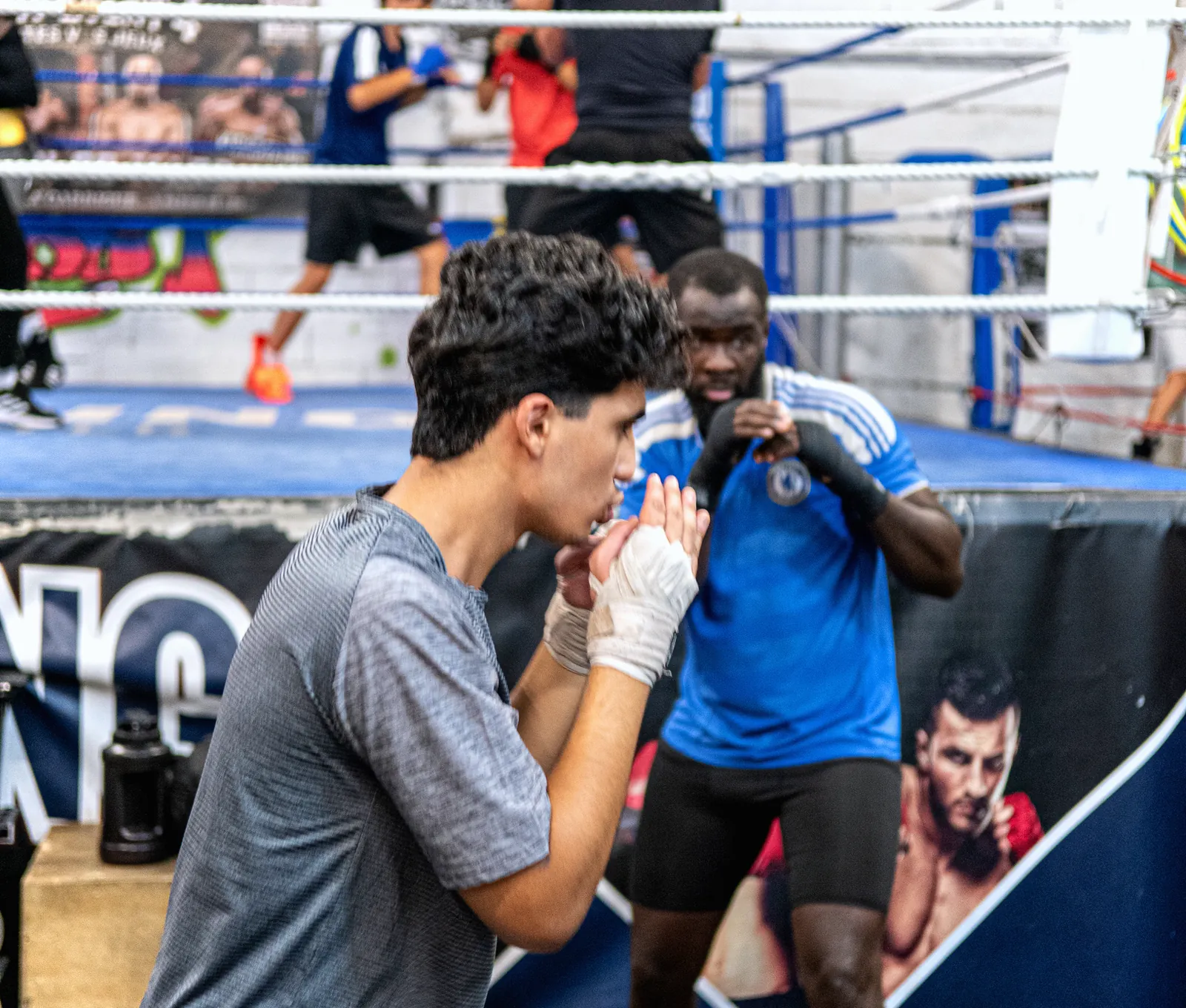 Un adolescent, mains bandées, en garde face à son coach au bord du ring