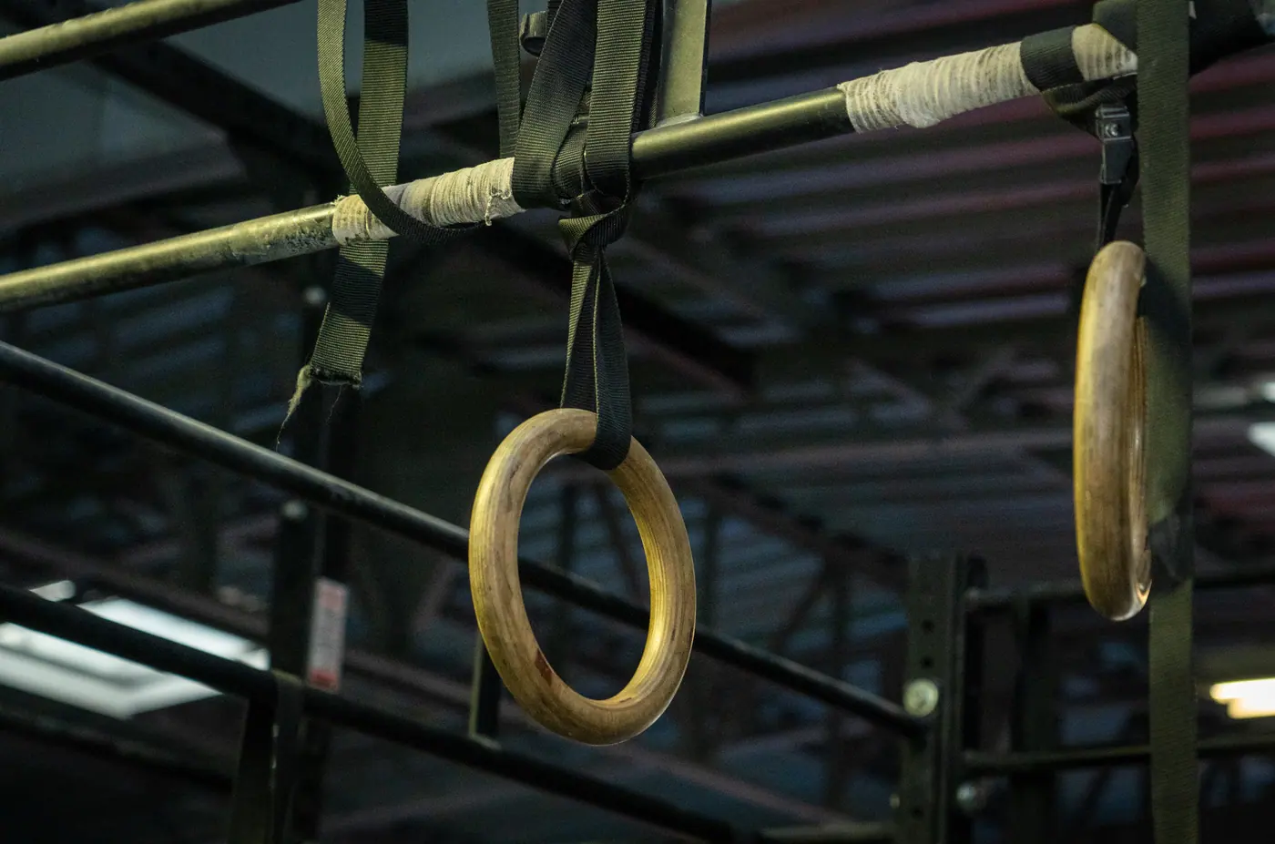 Deux anneaux de gymnastique en bois suspendus par des sangles à la structure métallique de la zone cross