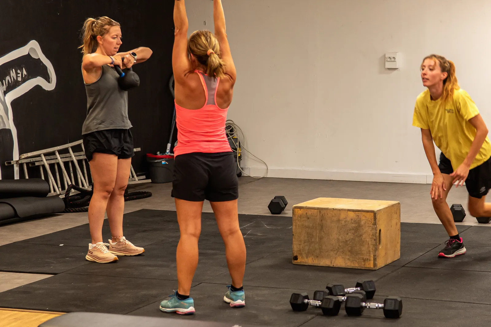 Trois pratiquantes enchaînent swing, développé et fentes autour d’un box en bois