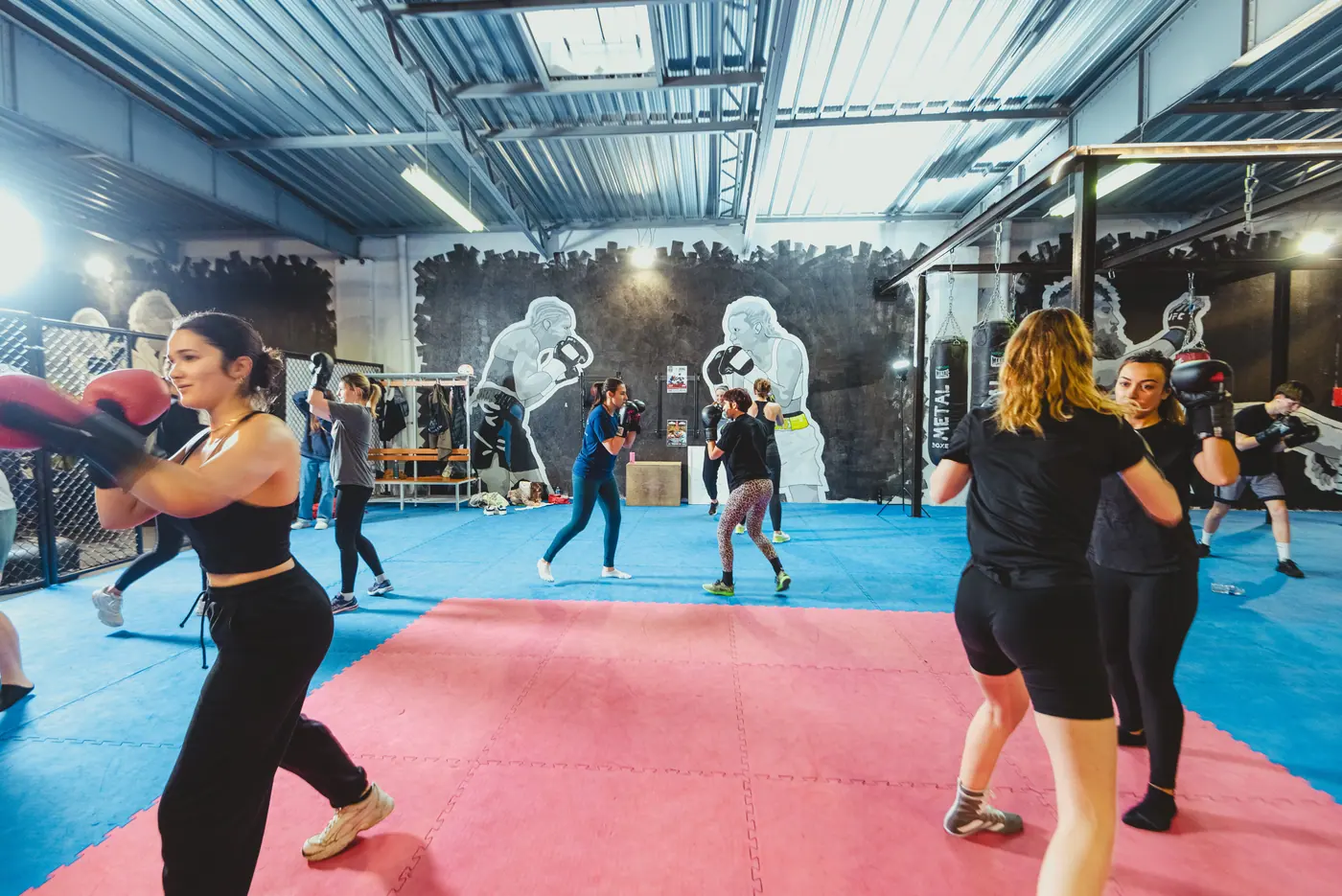 Un cours de boxe anglaise : des pratiquantes en garde travaillent aux boucliers sur le tapis bleu et rouge