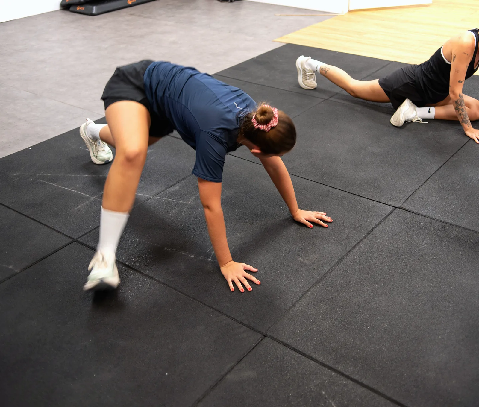 Deux pratiquantes enchaînent un exercice de gainage à quatre pattes sur les dalles noires