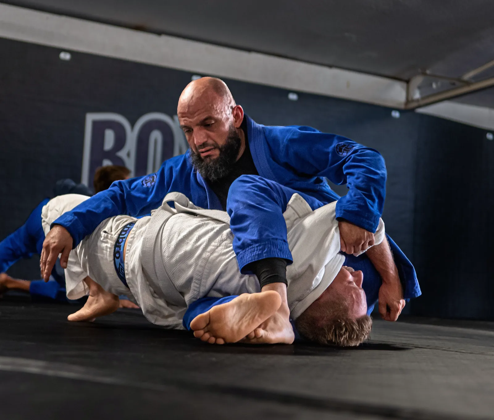 Un pratiquant en kimono bleu maintient son partenaire au sol sous lui, appuis bien écartés
