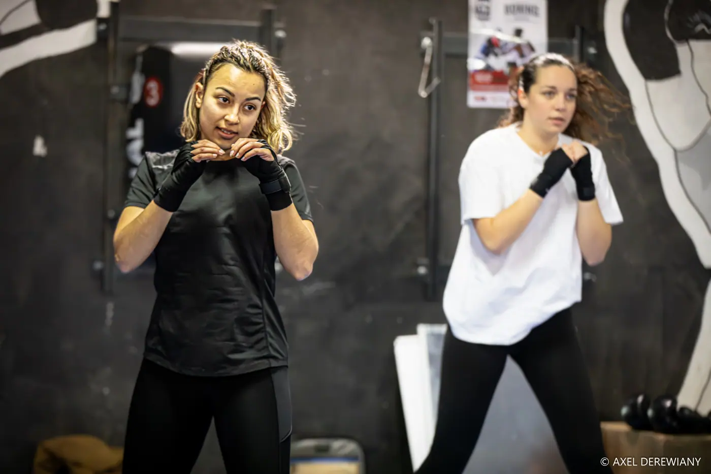 Deux pratiquantes en garde, mains bandées de noir, devant un mur peint