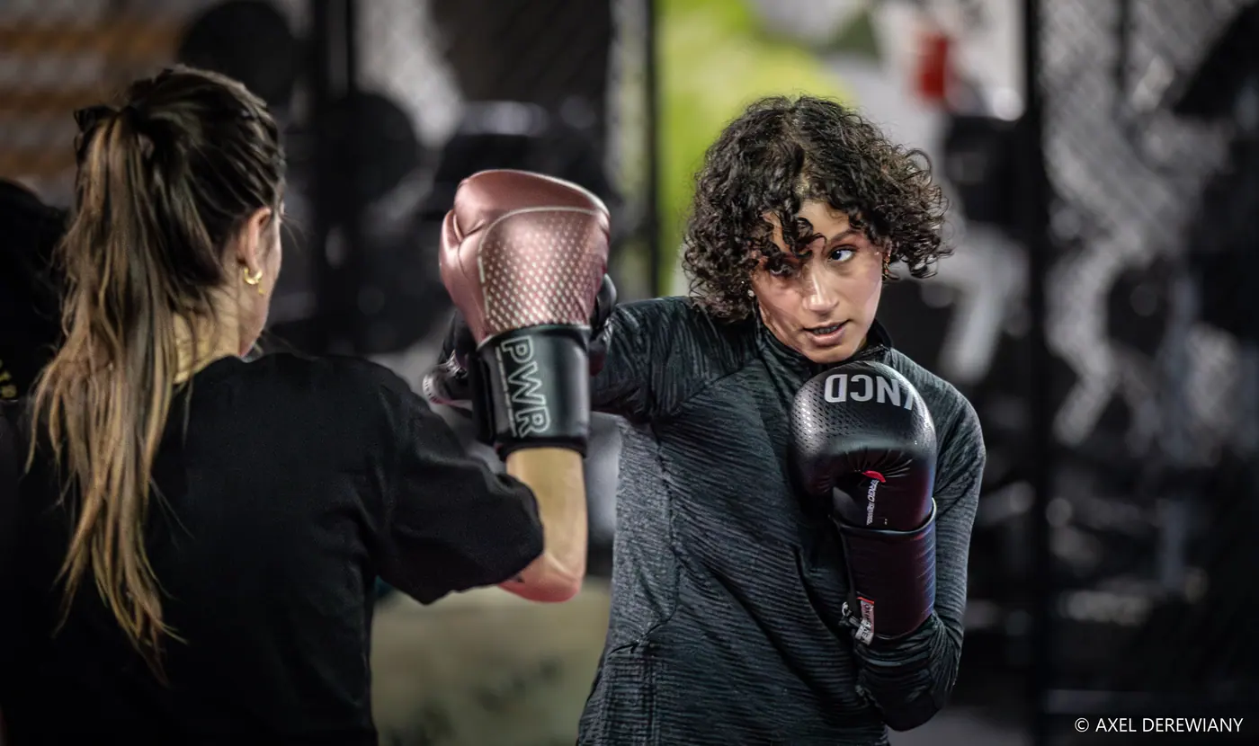 Deux pratiquantes face à face, l’une en gants roses, l’autre aux cheveux bouclés en gants noirs