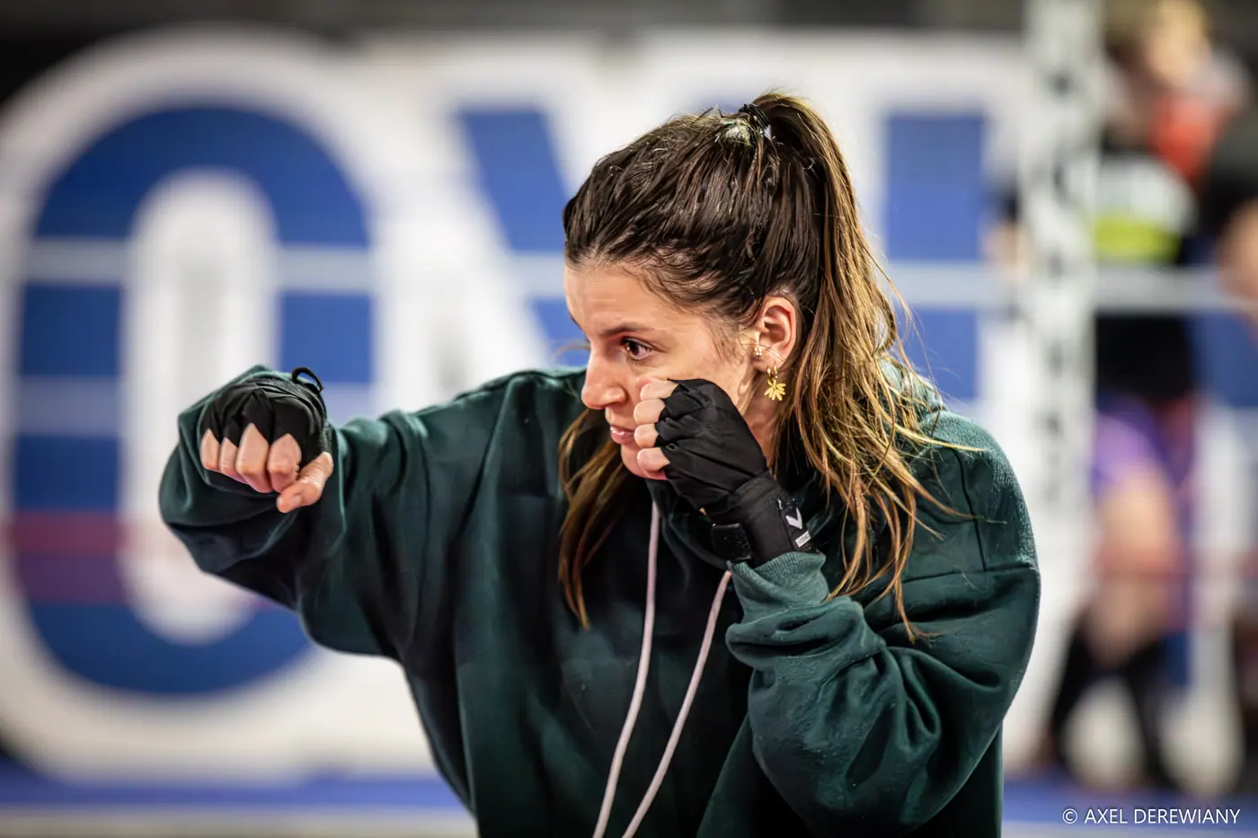 Une pratiquante en sweat vert, mains bandées, garde haute et regard fixé devant elle