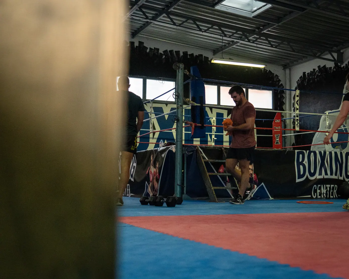 Le ring Boxing Center vu entre deux sacs de frappe, un pratiquant à la corde au premier plan